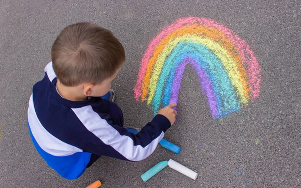Bir çocuk asfalta bir gökkuşağı çizer. Seçici odaklanma. çocuk.