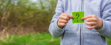 Çocuğun elinde parkın arka planında soru işareti olan çıkartmalar var. Doğa. seçici odak