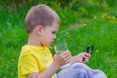 Çocuk bir bardakta büyüteçle suyu inceler. Seçici odaklanma. Çocuk.