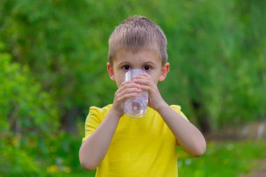 The boy drinks water from a glass. Pure water. Summer. selective focus