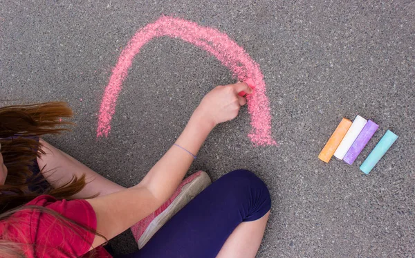 girl draws a rainbow, sun, car with chalk on the asphalt. Selective focus