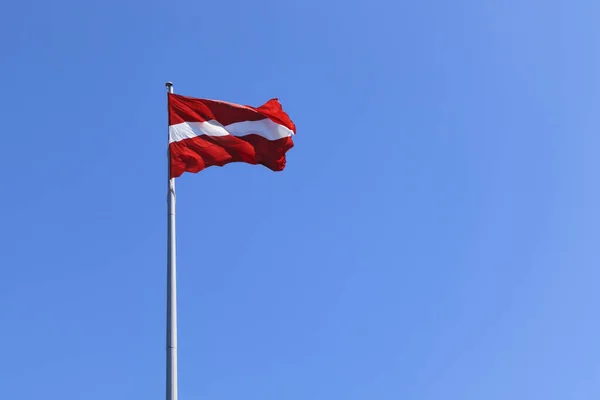 Mavi gökyüzünün arka planında Letonya ulusal bayrağı