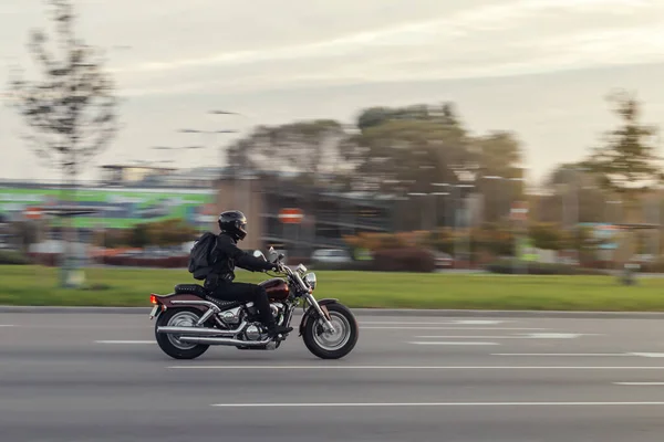 A motorcycle rides on the street at high speed in front of the rising sun. The motorcyclist dressed in all black. Motion blur.