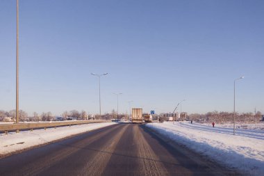 Kışın yolda giden bir arabanın ön camından bakmak. Yol kenarında kalın bir kar tabakası, yolda ıslak asfalt..