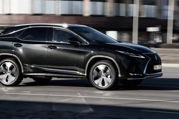 Koyu renkli Lexus RX Hybrid caddede ilerliyor. Yan görüş. Riga, Letonya - 16 Mar 2022.