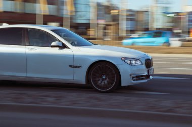 Beyaz bir araba yüksek hızda caddede sürüyor. Arabanın ön tarafının görüntüsü. Beyaz BMW 7 Serisi. Riga, Letonya - 16 Mar 2022