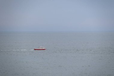 Denizde küçük, kırmızı bir balıkçı teknesi. Sisli deniz, fırtınadan kısa süre önce bulutlu hava.