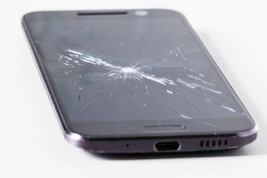 Beyaz bir masada yırtık bir ekranı olan akıllı bir telefon. Çatlak ekran