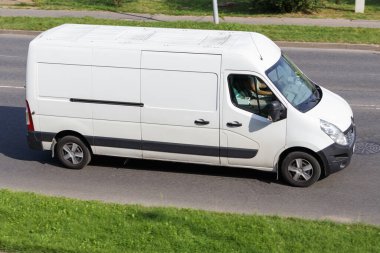 A white cargo van is driving on an asphalt street.