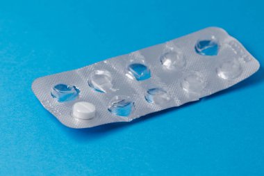 Tek tabletli bir paket ilaç. İlaç kullanımı, mavi arka planda kullanılmış ilaç şişliği. Yumuşak odak.