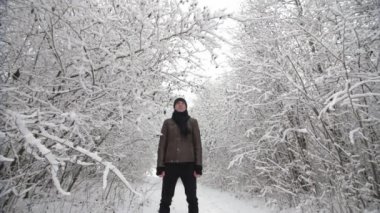 Yetişkin bir adam, karla kaplı ağaçların altında durur ve yavaş çekimde kar yağar..