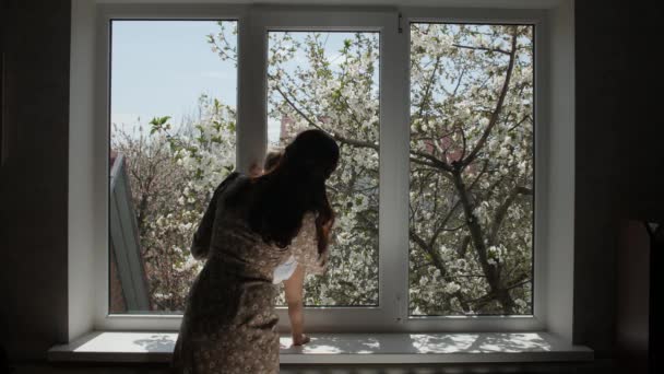 Українська мати з немовлям наближається до білого вікна.. — стокове відео