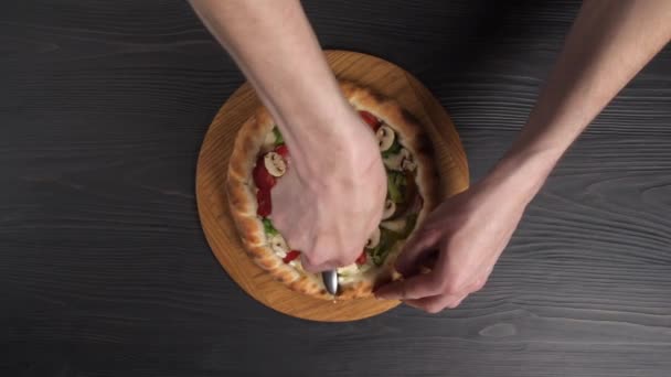 Manliga händer skära pizza med pizza kniv på trä bakgrund. — Stockvideo