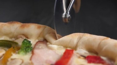 Pizza bıçağı taze bir pizzanın yüzeyinde yuvarlanır ve onu keser. Tekerlek hamuru geçirir ve ahşap koyu yüzey arka planını görebilirsiniz. Yakın çekim, yavaş çekim.