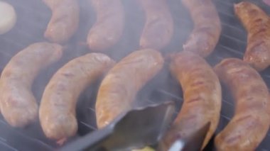 Barbekü tabağında lezzetli sulu sosisler. Metal maşaların yardımıyla siyah ızgarada kaynayan sosisleri pişiriyoruz. Duman var..