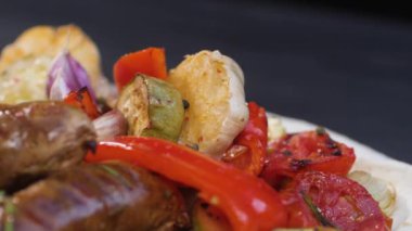 Yavaş çekimde biber düşmesi ve ızgara domuz sosisi, kabak, sarımsak, paprika ve domates için baharat. Ürün pide ekmeğinde yatıyor..