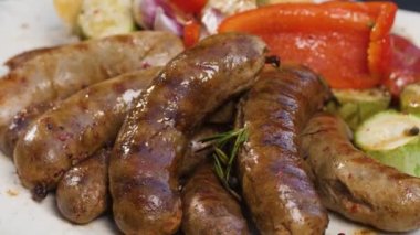 Fırında kabak, domates, sarımsak, paprika ile ızgara sosis yemeye hazır. Pita ekmeğinin üzerinde duran tabakta sosisten sebzeye kadar yiyecekler çeşitlidir..