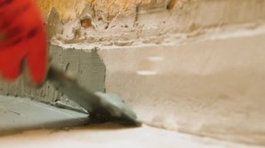 Bir işçinin yakın çekimi zemini duvarla sıkarken yere bir mala koyar. Kırmızı eldivenli bir el..