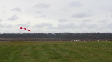A white single-engine light plane takes off from the runway. Against the background of an autumn landscape and windsock.