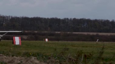 Tek motorlu beyaz bir uçak çimlerin üzerinde yavaşça ilerliyor. Sonbahar manzarasının arka planında. Yan görünüm.