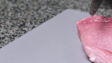 Chef slicing fresh pork tenderloin with a knife on a plastic gray board. Hands in black gloves. The camera is moving.