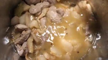 The cooks hand stirs pieces of lard and pork meat with a spoon in an iron pan. Cooking.