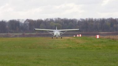 A white single-engine light plane slowly drives across the grass. On the background of an autumn landscape.