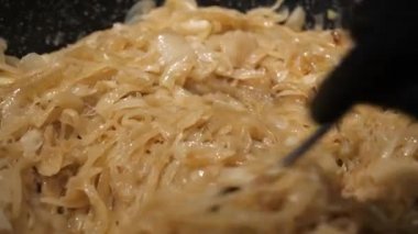 A cook in black gloves stirs fried golden onions in a pan with a spoon. the camera is moving