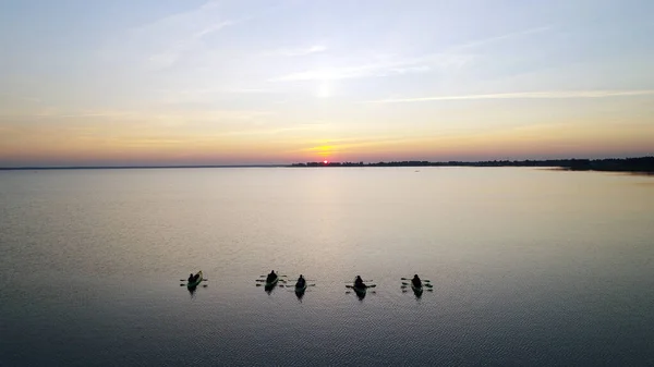 Five canoes with people stand on the water and wait for the sunrise. A large lake with a reflection of the colored sky.