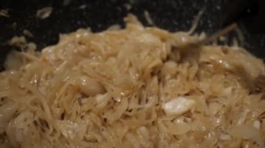 A cook in black gloves stirs fried golden onions in a pan with a spoon. the camera is moving