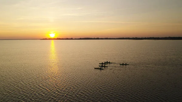 Five kayaks with people are sailing towards the sunrise. A large expanse of lake water. Summer morning. Aerial view of Ukraine.