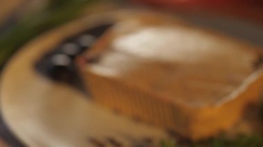 On a gray plate lies a large piece of pate decorated with dill stalks, black olives, and black pepper.