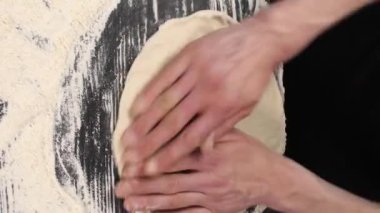 Dikey video. Restoranda İtalyan pizzası pişirmek. Ellerinle çiğ pizza hamuru uzatıyorsun. Profesyonel bir aşçı elleriyle İtalyan pizza hamurunu gerer ve büker..