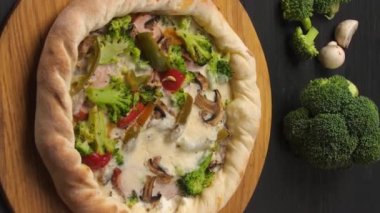 Dikey video. Koyu kahverengi bir masada içindeki malzemelerle pizza sunumu. Jambon, kırmızı biber, mantar ve peynir var. Bardakta kremalı sos..