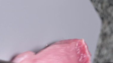 Dikey video. Şef, plastik gri bir tahtada taze domuz filetosu dilimliyor. Siyah eldivenli eller..