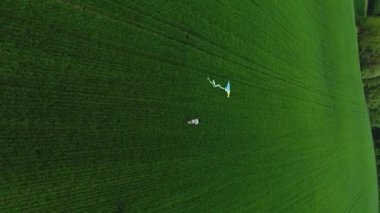 Dikey video. Çocuk buğday ekinleriyle tarlayı koşarak geçiyor. Elinde bir uçurtma tutuyor, sarı-mavi, arkasında uçuyor. Hava görünümü.