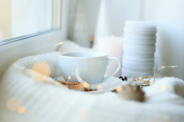Чашка кави над гірляндами різдвяних боке в будинку на столі з светром на задньому плані та прикрасами. Зимовий настрій, святкова прикраса, чарівне Різдво . — стокове фото