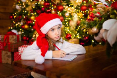 Mutlu Noeller ve mutlu tatiller. Noel Baba şapkalı küçük bir kız Noel Baba 'ya mektup yazar ve evde yeni yıl ağacı hayal eder. Tebrik kartı, Noel konsepti..