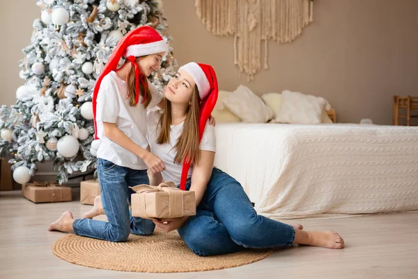 Сестры празднуют зимние праздники. Девушки обмениваются рождественскими подарками возле елки. Счастлив среди новогодних украшений. Лицензионные Стоковые Изображения