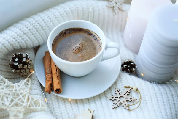 A cup of coffee over Christmas bokeh garlands in the house on the table with a sweater in the background and decorations. Winter mood, festive decoration, magical Christmas. — Stock Photo, Image