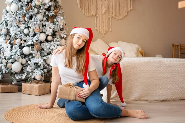 Сестры празднуют зимние праздники. Девушки обмениваются рождественскими подарками возле елки. Счастлив среди новогодних украшений. Лицензионные Стоковые Фото