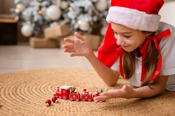 Счастливый ребенок в красной шляпе играет с игрушечным древесным поездом под елкой Стоковое Фото