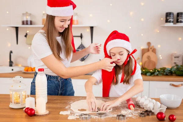 Дети готовят рождественское печенье на уютной кухне. Сестры вместе готовят праздничную трапезу для семьи. Милые девочки пекут, играют и дурачатся с мукой. Концепция детского повара Лицензионные Стоковые Изображения