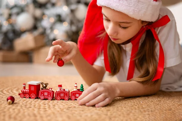 Счастливый ребенок в красной шляпе играет с игрушечным древесным поездом под елкой Стоковое Изображение