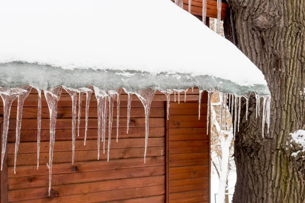 Eiszapfen hängen vom Dach eines Holzhauses. lizenzfreie Stockbilder