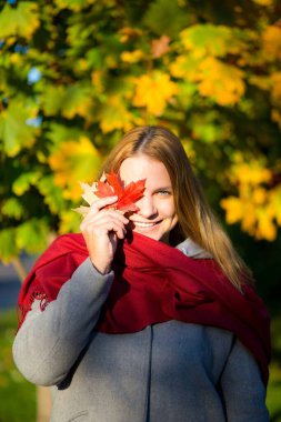 Gri paltolu genç bir kız ve elinde bir akçaağaç yaprağı olan kırmızı bir eşarp.