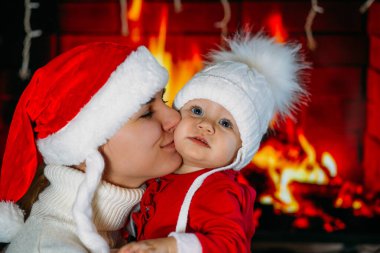 Yeni yıl şapkalı bir anne, kırmızı elbiseli bir kızı şöminenin arka planında tutuyor.