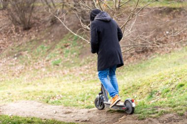 Hipster parkta elektrikli bir scooterla yol boyunca gider.