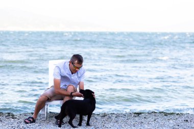 Kumsalda güneşlenirken köpekle oynayan mutlu genç adam..