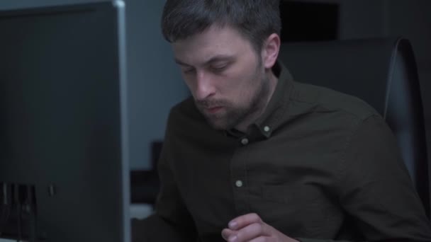 Głęboko w strefie wydajności. Mężczyzna w koszuli pracuje przy komputerze, pisze na klawiaturze i patrzy na monitor z ostrością wieczorem. Wyczerpany programista. Praca w domu — Wideo stockowe